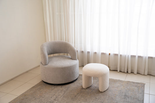 כורסה מעוצבת עם הדום מבד אפור בהיר בסלון מואר עם שטיח.