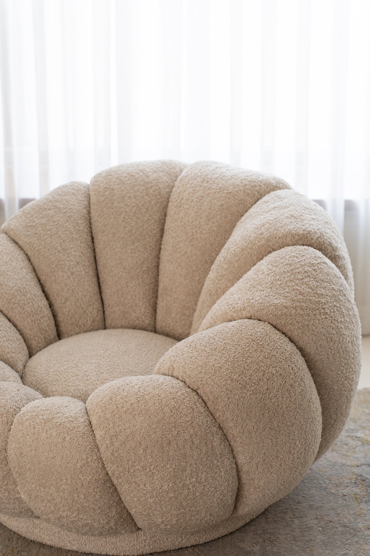 כורסה מעוצבת מבד בוקלה בצבע שמנת בזווית צד.