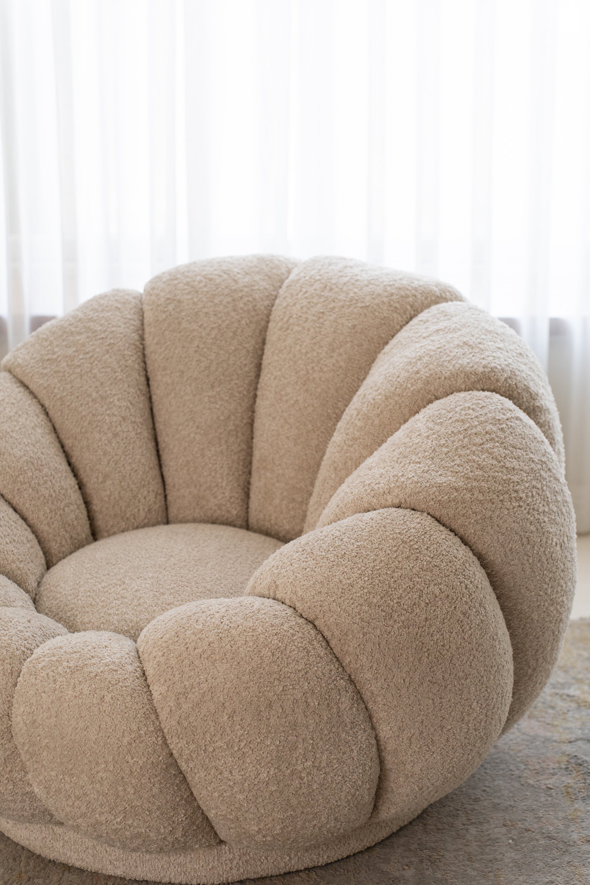 כורסה מעוצבת מבד בוקלה בצבע שמנת בזווית צד.