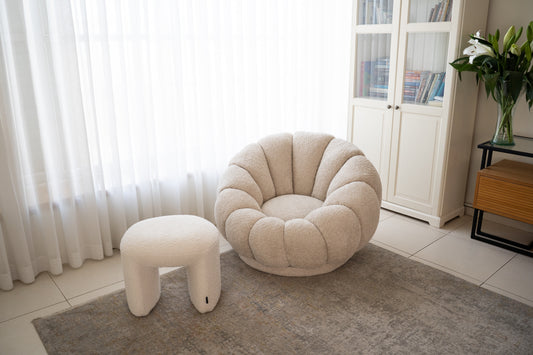 כורסה עגולה מבד בוקלה בצבע שמנת עם הדום תואם בפינת סלון מודרנית.