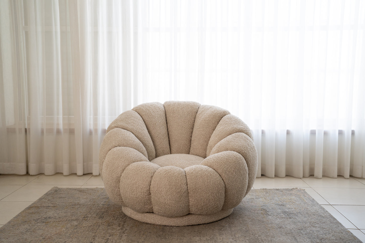 כורסה עגולה מבד בוקלה בצבע שמנת בפינת ישיבה ליד וילונות.