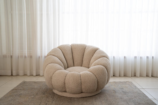 כורסה עגולה מבד בוקלה בצבע שמנת בפינת ישיבה ליד וילונות.